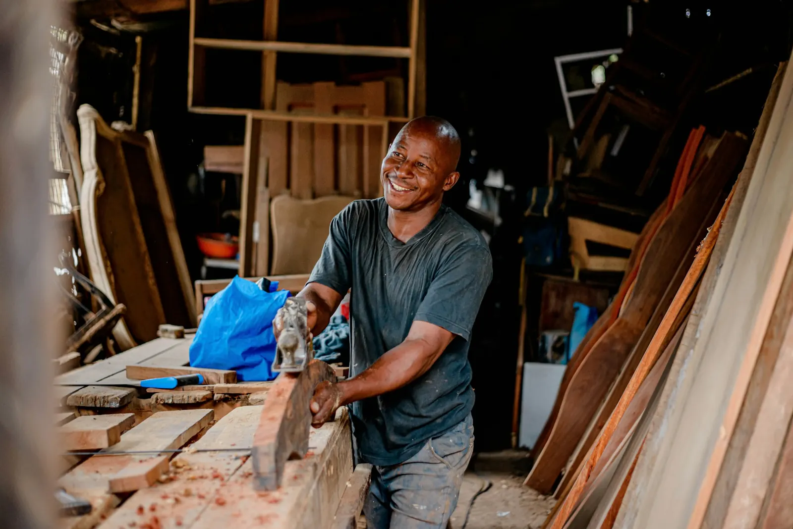 Le menuisier rabote une planche à l'établi, le sourire aux lèvres