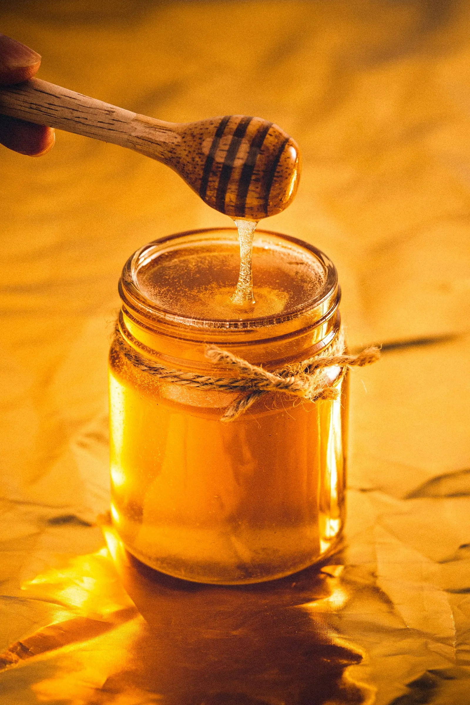 Une cuillère en bois laisse couler du miel doré dans un pot en verre